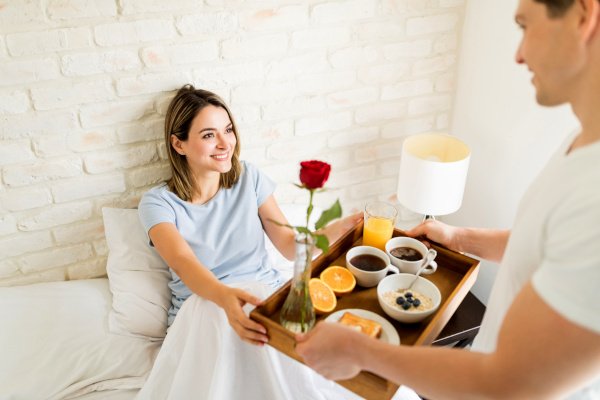 Smiling woman looking at husband serving breakfast to her in bed.