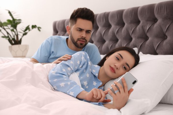 Woman ignoring her husband while using smartphone in bed at home.